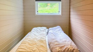 A narrow room with a single bed, a small window, and wooden walls.