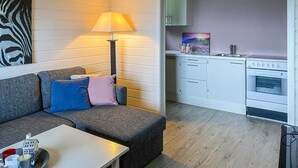 A compact living space with a sofa, a table, a lamp, a kitchen area with a stove, and a painting on the wall.