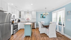 A modern kitchen with white cabinets, stainless steel appliances, and a wooden floor. - Cheerful 3BR/2BA - just steps to the beach! (Oak Island)