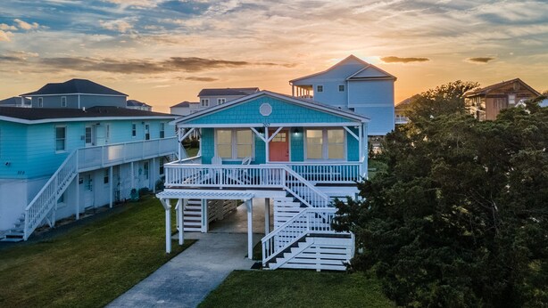 A two-story house with a balcony and a staircase leading to the entrance. - Cheerful 3BR/2BA - just steps to the beach! (Oak Island)
