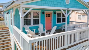 A turquoise and white beach house with a porch, white Adirondack chairs, and a red door. - Cheerful 3BR/2BA - just steps to the beach! (Oak Island)