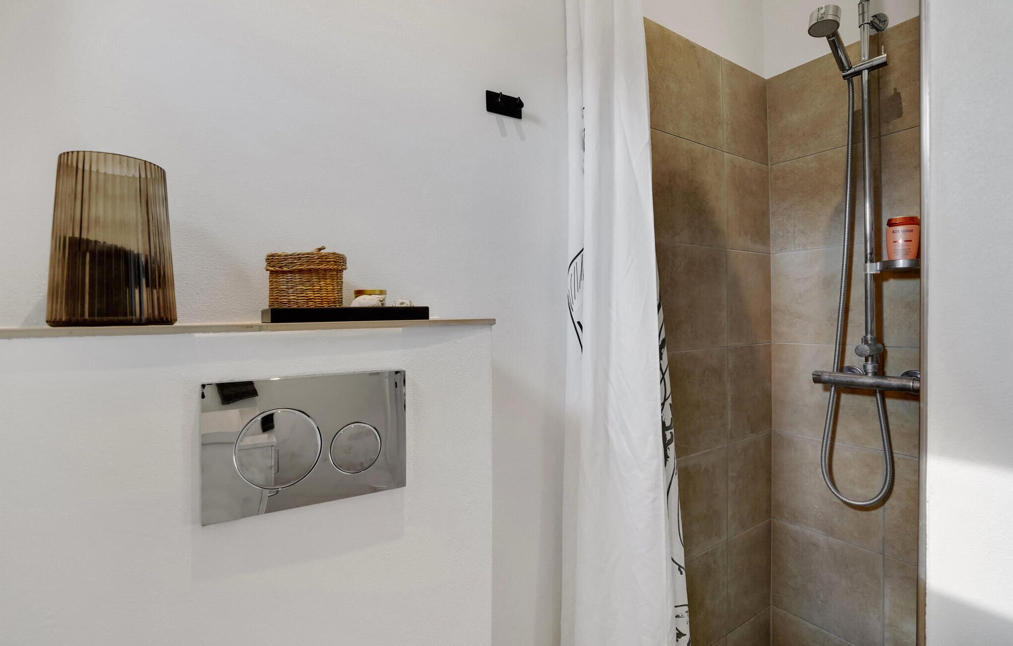 Un baño con ducha, un perchero y un estante con una cesta y un frasco.