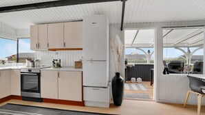 A modern kitchen with white cabinets, a built-in oven, and a large refrigerator. There is a dining area with a table and chairs, and a view of the outdoors through large windows. - Pet friendly home in Hejls with WiFi (Hejls)