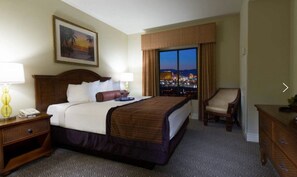 Relax in a spacious room with a large bed, nightstand, and comfortable chair, offering a city view.