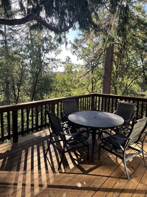 Une terrasse en bois avec une table ronde et quatre chaises, entourée d’arbres.