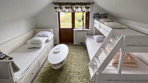 Un dormitorio con literas, una pequeña mesa redonda y un ventanal con cortinas.