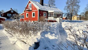 Una casa roja con un porche y una chimenea, rodeada de nieve.