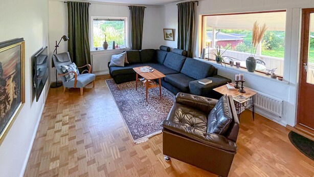 Una sala de estar con un sofá, un sillón y una mesa de centro. Hay una ventana con cortinas, un radiador y vistas a zonas verdes.