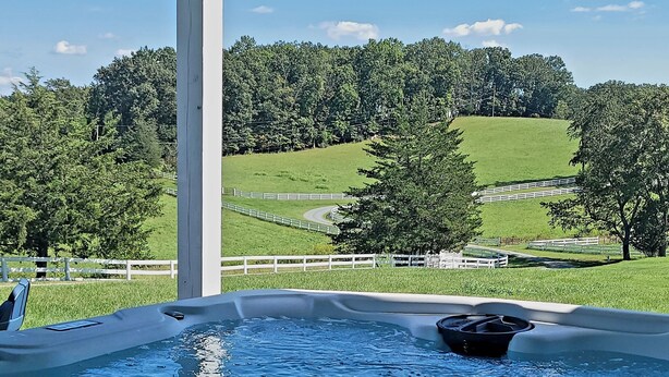 A hot tub with a view of a green landscape and a white fence.