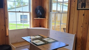 A wooden interior with a bench and table, large windows, and a fan.