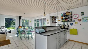 Une cuisine moderne dotée d’un îlot central, d’un coin repas avec des chaises et d’une vue sur le jardin grâce à de grandes fenêtres.