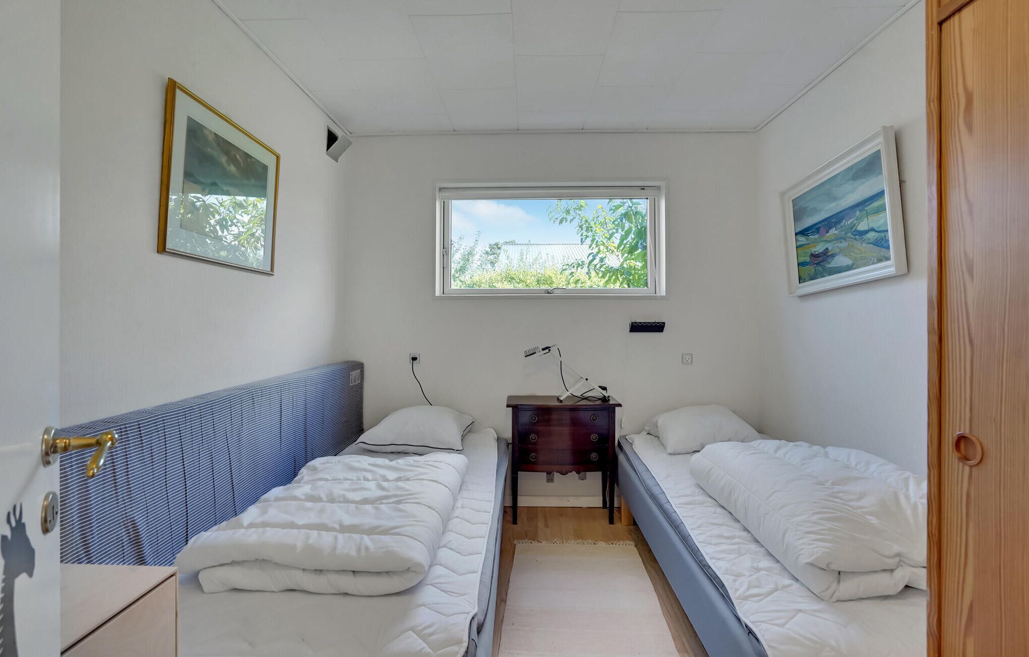 Ein kleines, gut beleuchtetes Zimmer mit zwei Einzelbetten, einem kleinen Tisch und einem Fenster, das natürliches Licht hereinlässt.