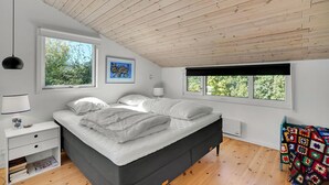 Une chambre à coucher moderne avec un grand lit, deux fenêtres, une table de chevet et une couverture colorée.