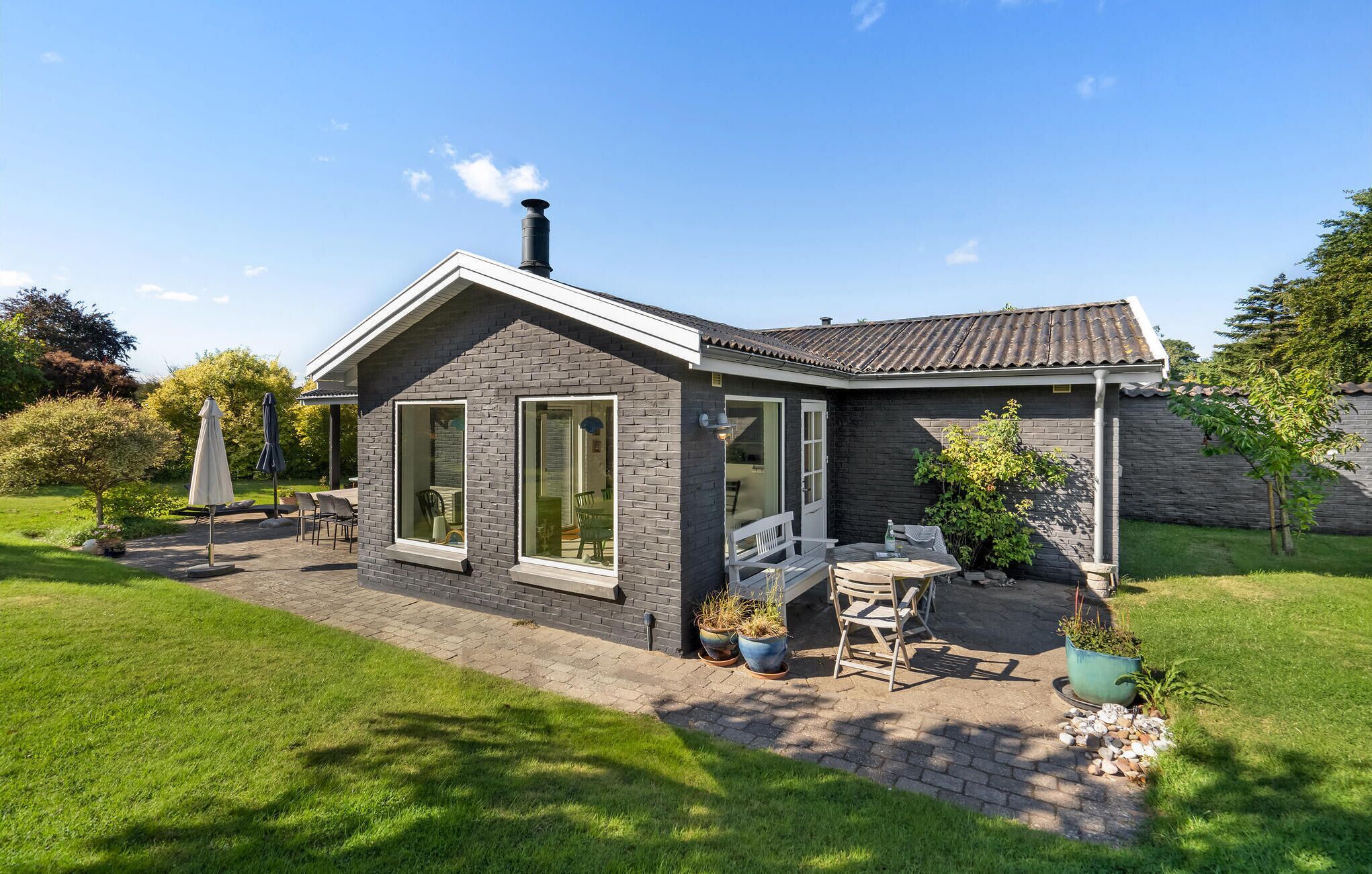 Ein modernes Haus mit Ziegelaußenwand, großen Fenstern und einer Terrasse mit Gartenmöbeln.