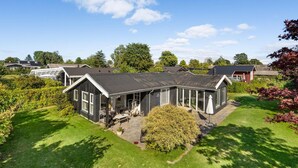 Une maison moderne dotée d’un grand patio, entourée d’une végétation luxuriante et surplombant un ciel d’un bleu éclatant.
