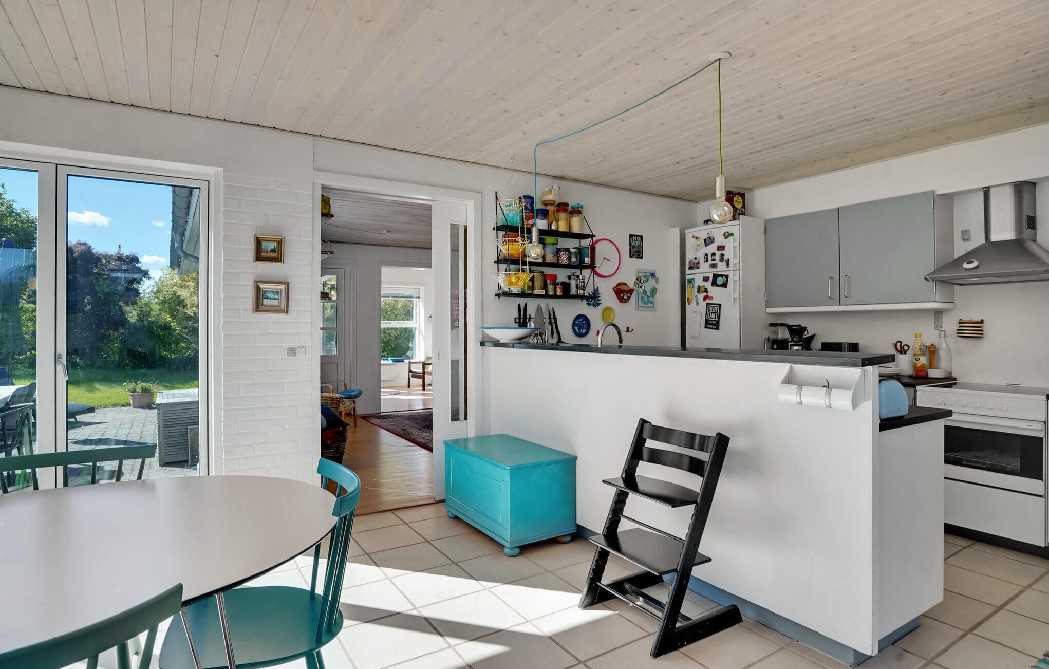 Una cocina moderna con armarios blancos, una isla central y un comedor con una mesa y sillas turquesas.