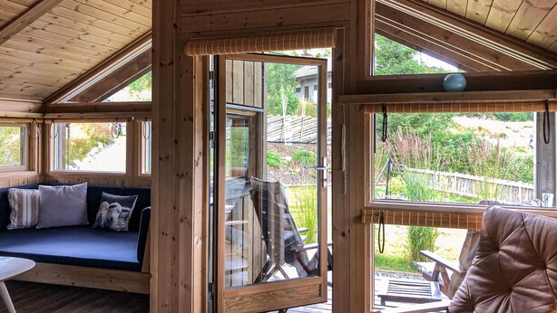 A wooden cabin interior with a sofa, a dining table, and a view of the outdoors.