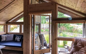 Een houten chalet van binnen met een bank, een eettafel en uitzicht op de omgeving.