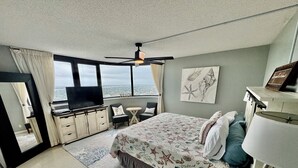 Ein Hotelzimmer mit Bett, Fernseher, Schreibtisch, Stuhl, kleinem Tisch und Blick auf die Stadt.