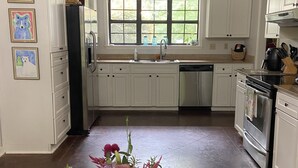 Eine Küche mit weißen Schränken, einem Edelstahl-Kühlschrank, einem Fenster mit Aussicht und einer Vase mit Blumen auf der Arbeitsfläche.
