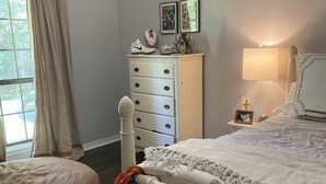 Ein Schlafzimmer mit einem Bett, einem Nachttisch, einer Kommode und einem Fenster mit Vorhängen.