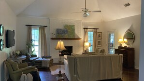 Ein geräumiges Wohnzimmer mit Kamin, Deckenventilator und Wandfernseher.