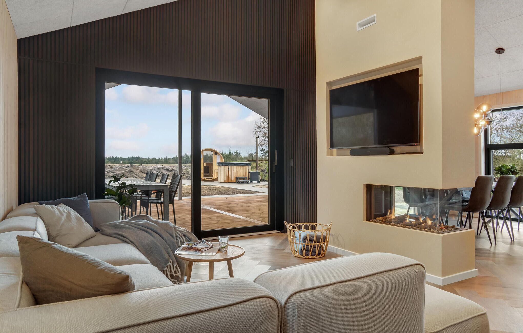 Una sala de estar moderna con un amplio ventanal corredera que da a un espacio exterior, una chimenea y un televisor de pantalla plana montado en la pared.
