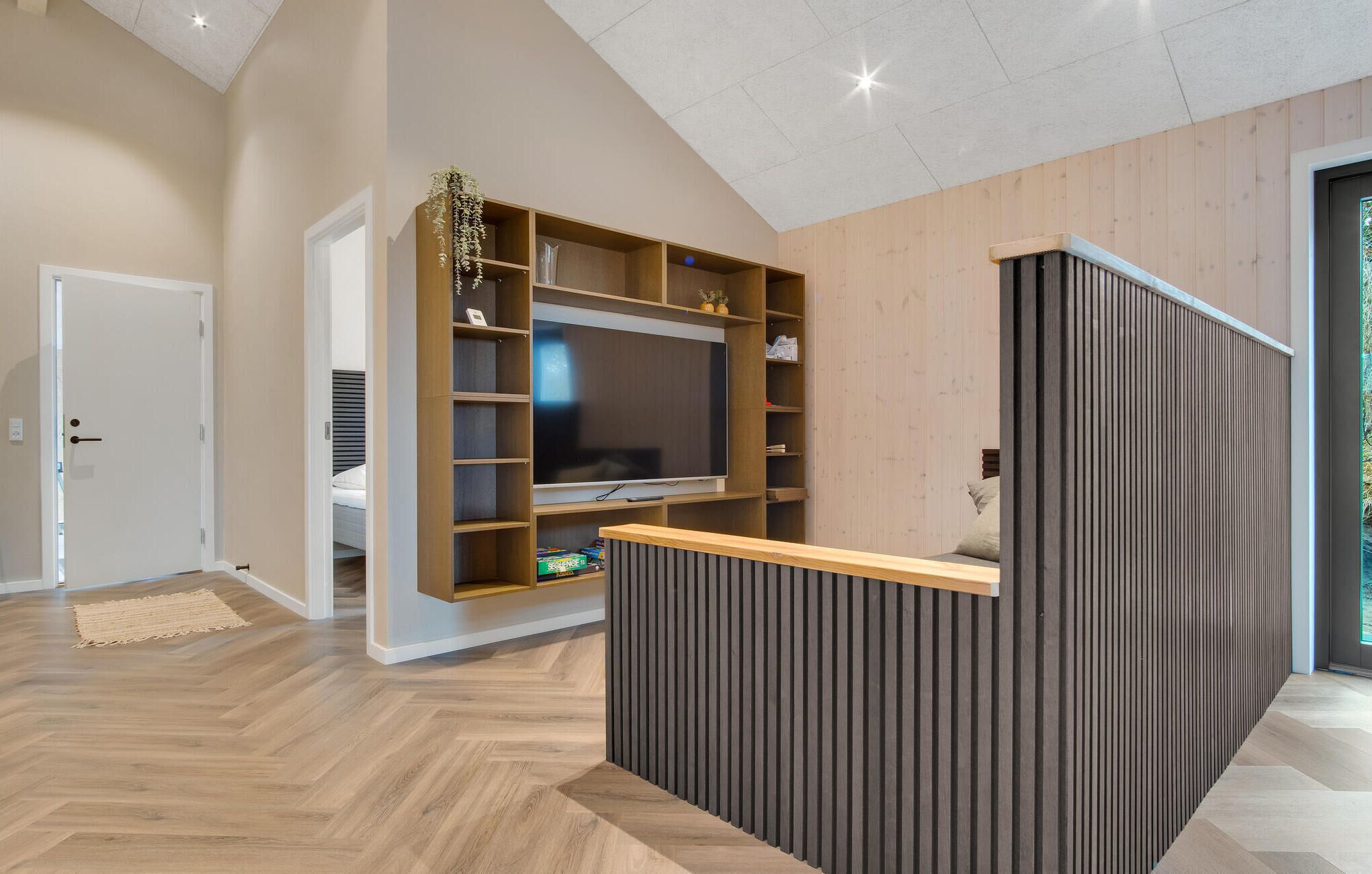 Un salon moderne doté d’un téléviseur encastré, d’étagères en bois et d’un petit coin salon.