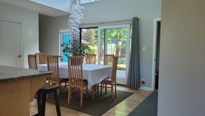A dining area with a table set for four, wooden chairs, a potted plant, and a view of greenery outside. - Modern, spacious four-bedroom home on quiet street (Seattle)