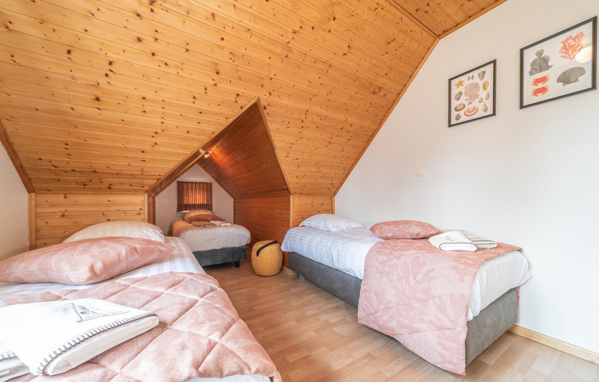 A cozy attic bedroom with wooden sloped ceilings, two beds with pink bedding, and a small round table.
