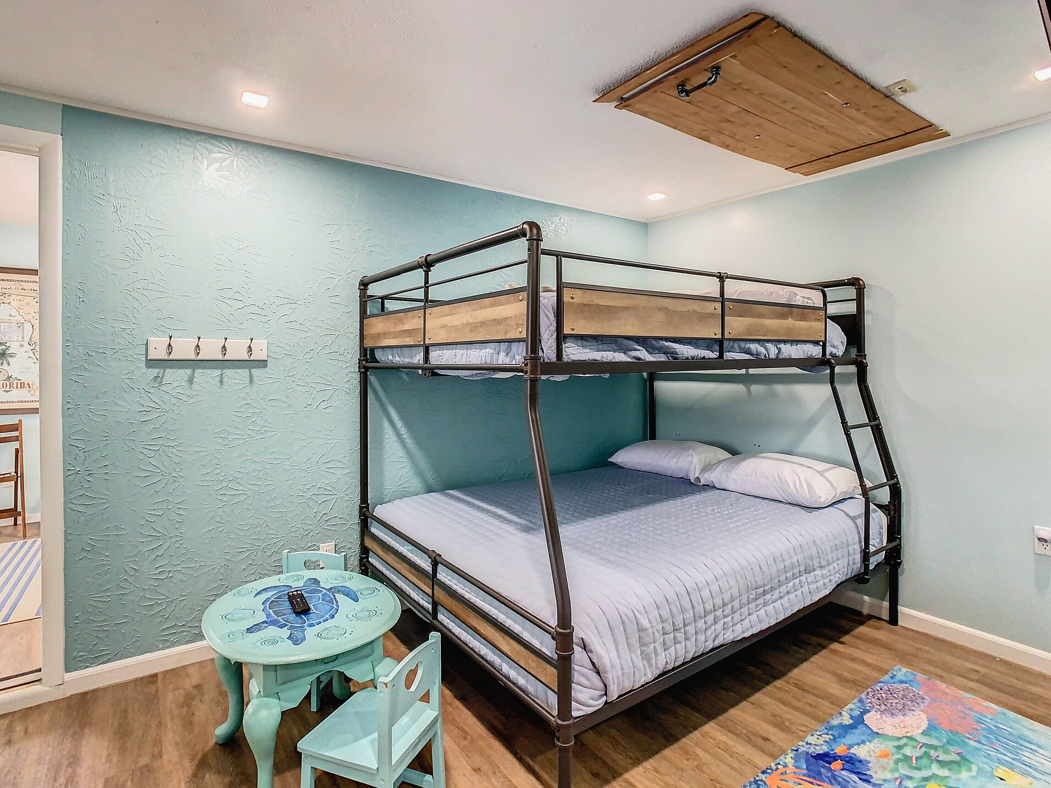 A bunk bed room with a wooden ceiling, a small round table with chairs, and a colorful rug on the floor.