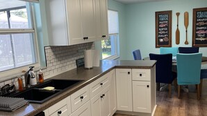 A modern kitchen with white cabinets, a black sink, and a wooden dining table with chairs. - 3/2 HEATED POOL HOME ON DEEP WATER CANAL (Crystal River)