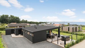 Un bâtiment moderne doté d’une terrasse et d’un espace extérieur aménagé pour s’asseoir, entouré d’autres immeubles résidentiels et d’un lac.