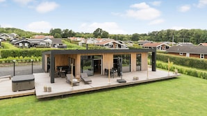 Un espace patio extérieur moderne, doté de sièges et d’un jacuzzi, entouré d’une pelouse bien entretenue et avec des immeubles résidentiels en arrière-plan.