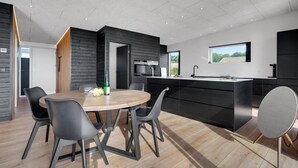Une cuisine moderne dotée d’un îlot central, de meubles de rangement noirs et d’un coin repas avec une table ronde et des chaises.