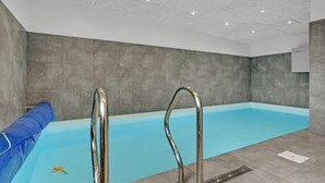 An indoor swimming pool with clear water, metal pool ladders, and a blue slide.