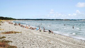 A pebbled beach with people sunbathing and swimming in the water.