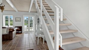Una habitación amplia con una escalera blanca, un ventanal grande y un rincón de descanso acogedor.