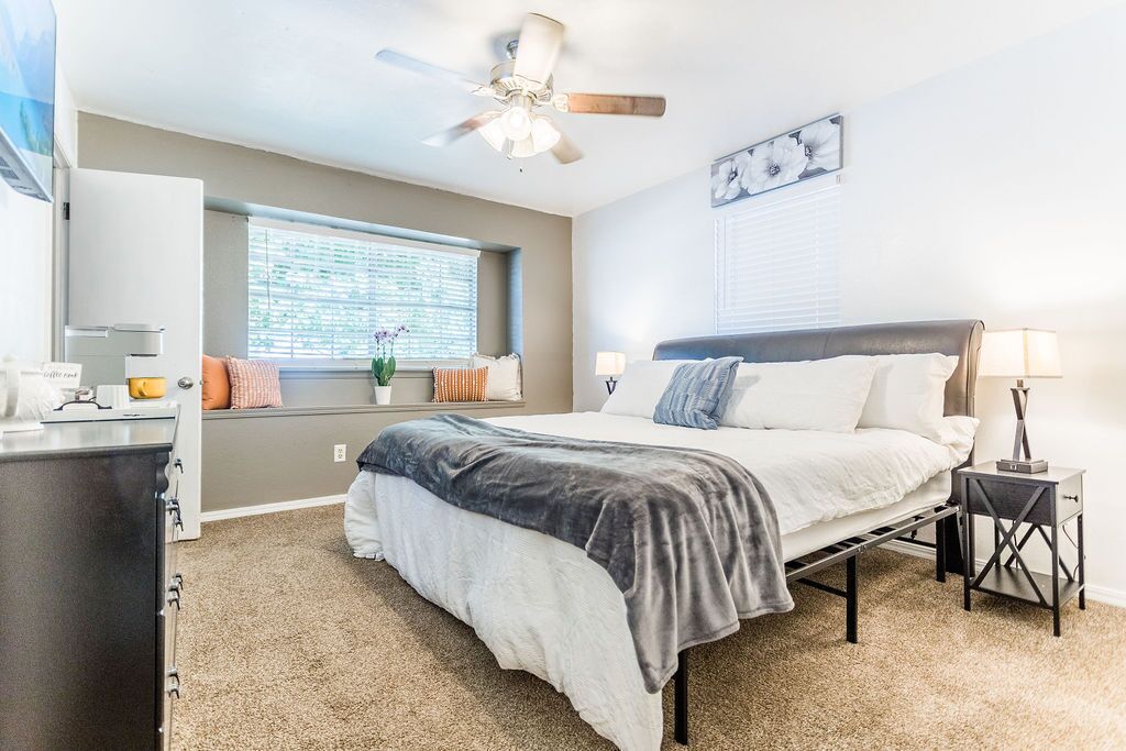 A bedroom with a bed, bedside table, nightstand, ceiling fan, window, and a wall-mounted artwork.