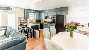 Une cuisine moderne avec des armoires de couleur turquoise, un îlot central et un coin repas comprenant une table et des chaises blanches.