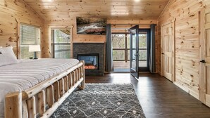 Interno di una baita in legno con un letto, un camino e vista panoramica attraverso una porta in vetro.