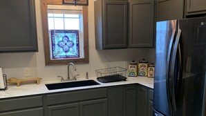 Une cuisine moderne avec des meubles de couleur sombre, un réfrigérateur en acier inoxydable, une fenêtre ornée de vitraux et un plan de travail en bois.