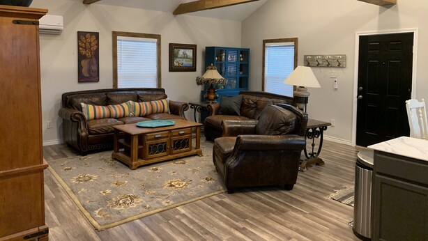 Un salon spacieux avec un plafond haut, des poutres apparentes, un canapé en cuir marron, une table basse en bois et un tapis à motifs.