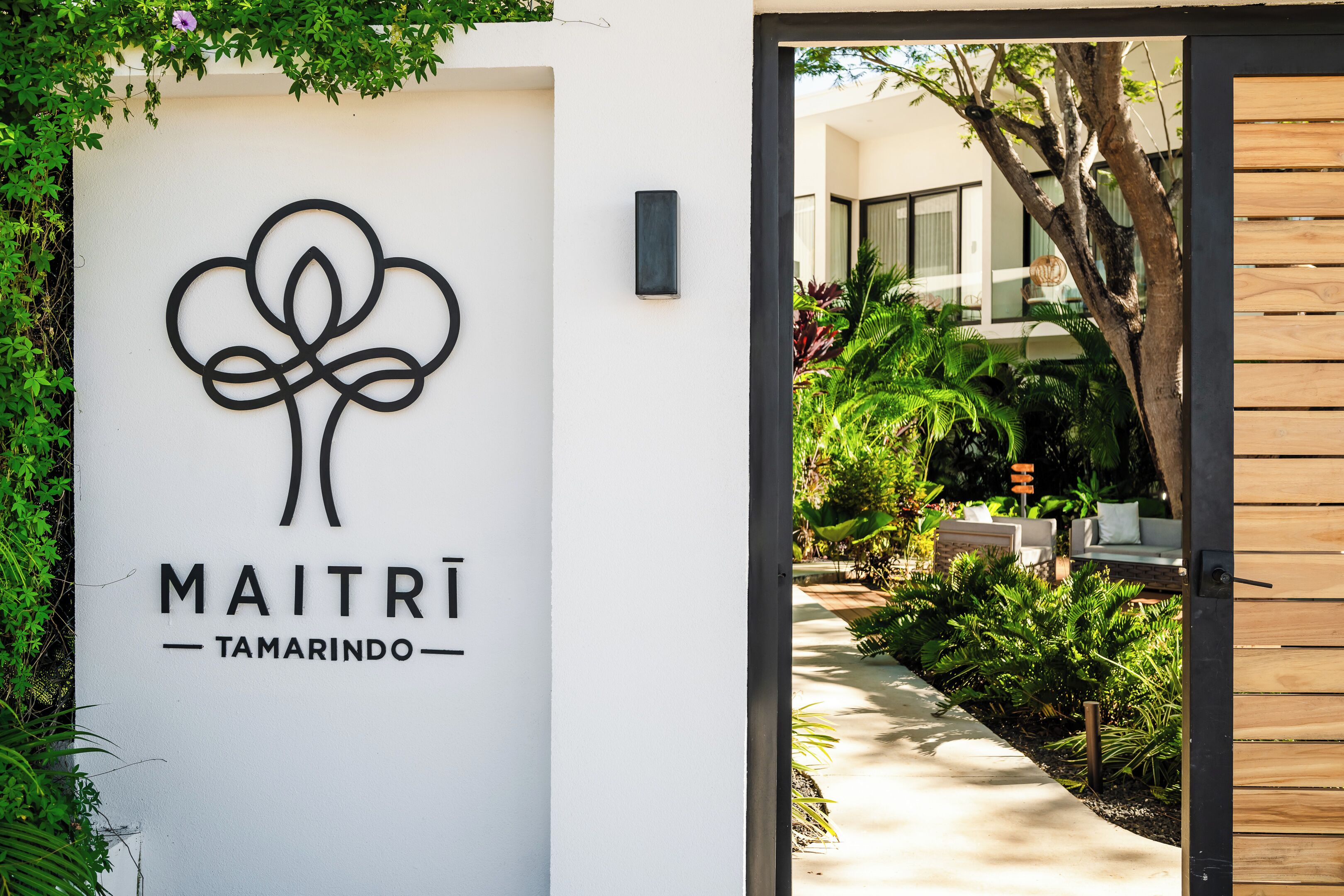 Une enseigne pour « MAITRI TAMARINDO », avec un logo stylisé, un chemin menant à un bâtiment et une végétation luxuriante.