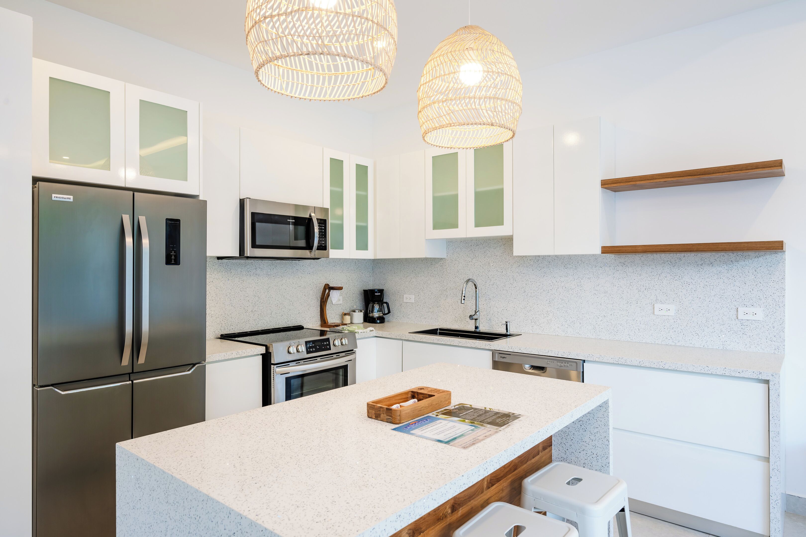 A modern kitchen with white cabinets, stainless steel appliances, a granite countertop, and wicker pendant lights.