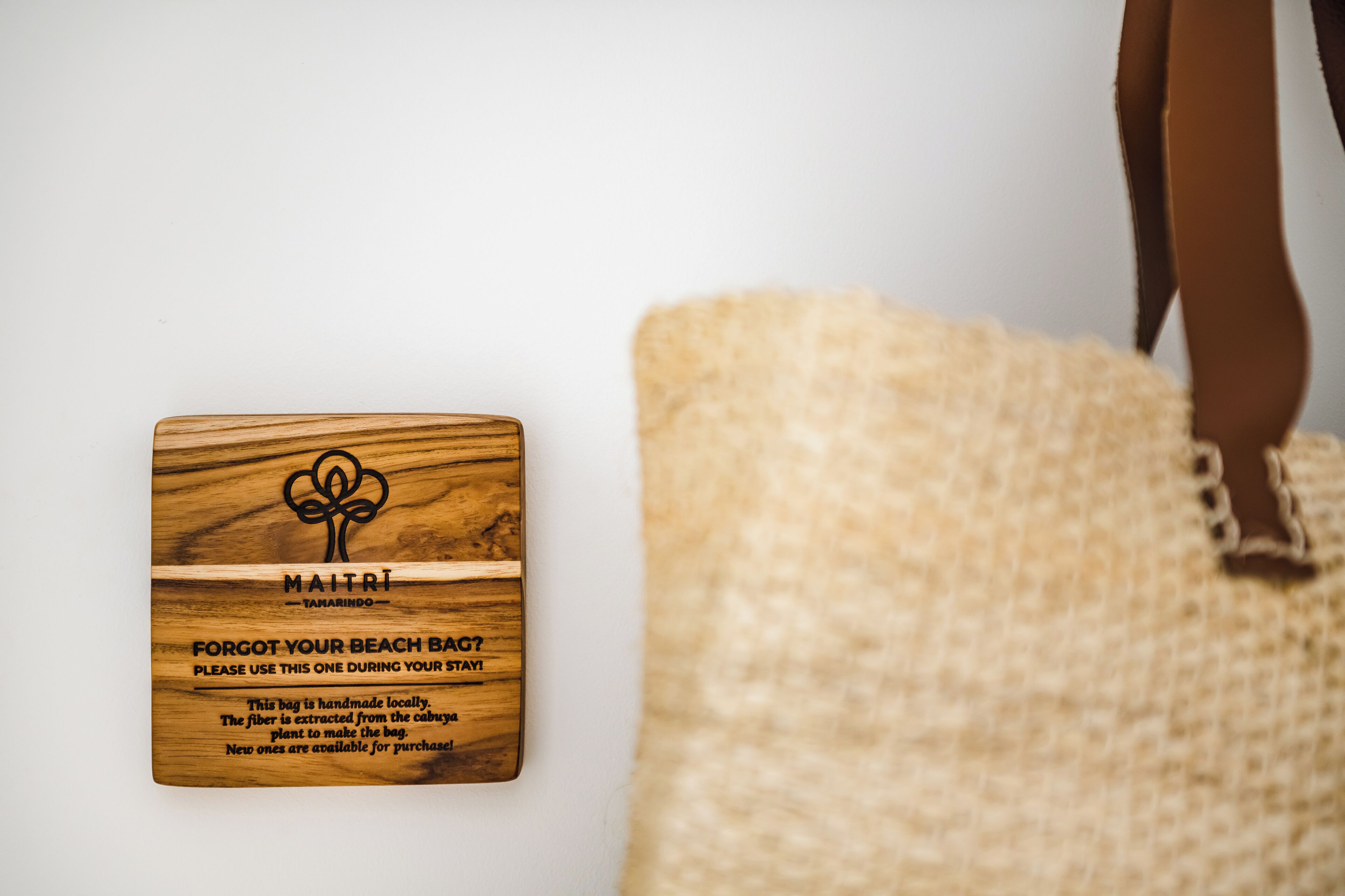 A wooden tag with text and a logo, placed next to a beige textured bag.