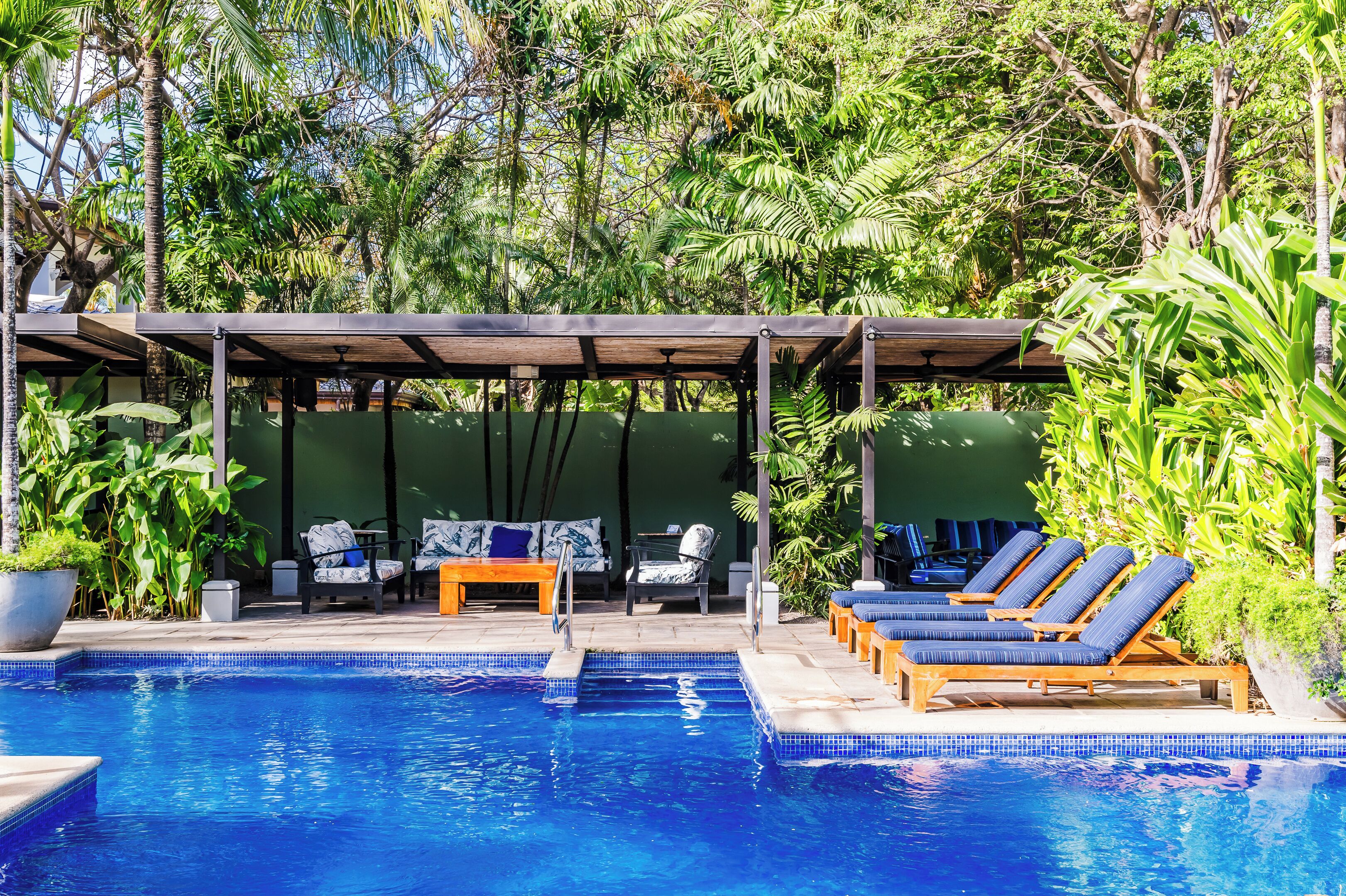A pool area with lounge chairs and a covered seating area surrounded by lush greenery.