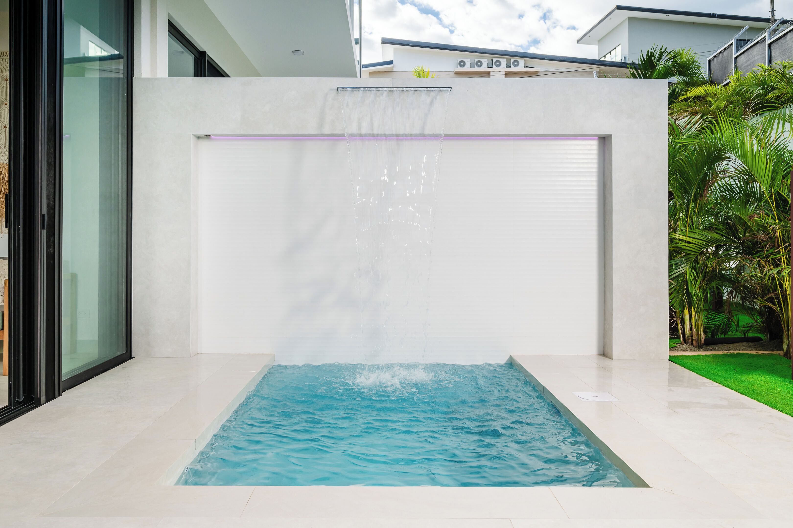 Une piscine intérieure moderne agrémentée d’une cascade, entourée d’un décor minimaliste et protégée par une paroi de verre.