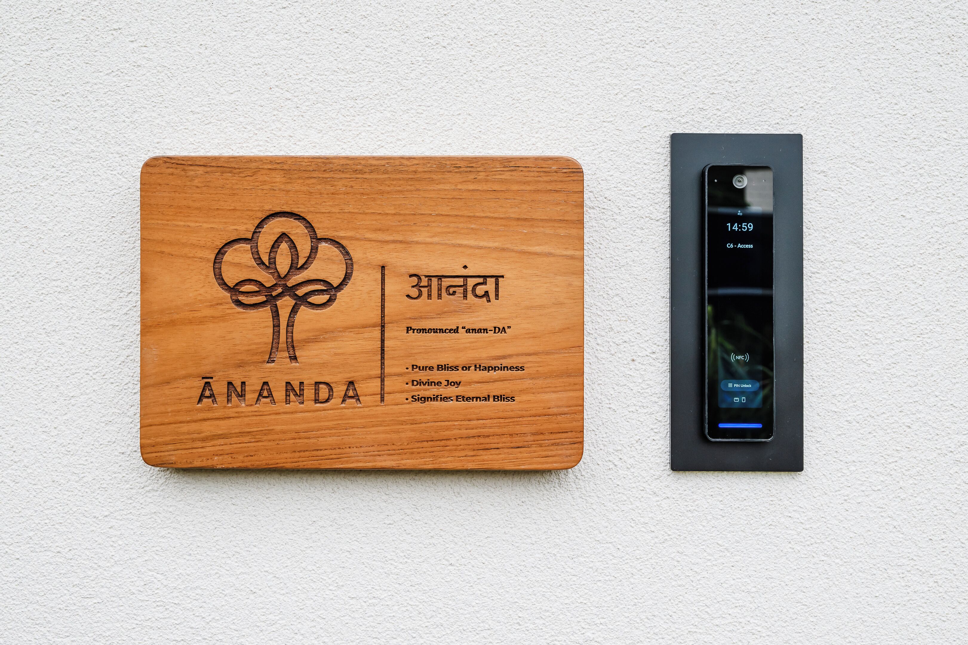 Une plaque en bois portant le nom « Ananda » et un téléphone intelligent fixé au mur.