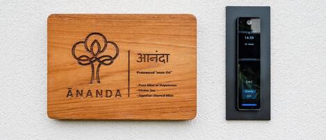 Une plaque en bois portant le nom « Ananda » et un téléphone intelligent fixé au mur.